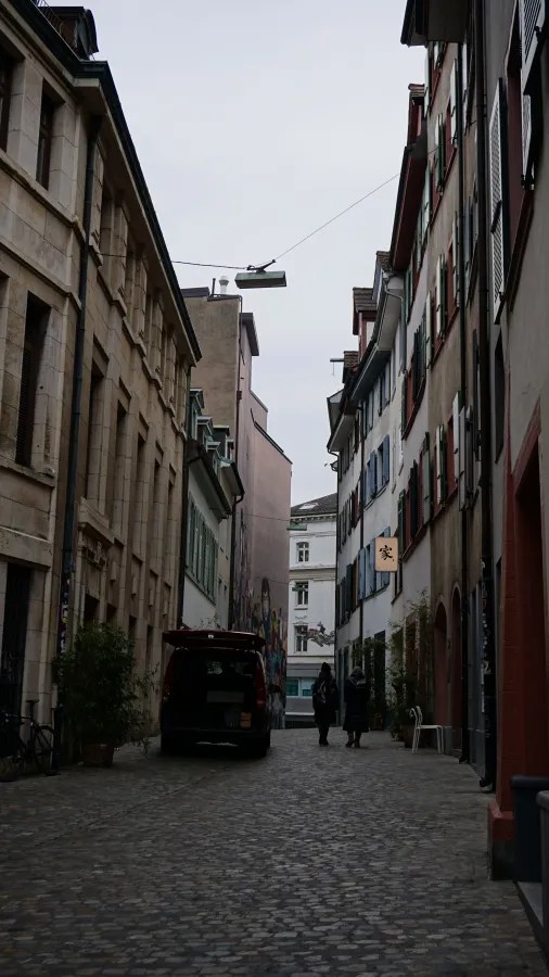 Two people walking down a narrow cobblestone street between tall, historic buildings.