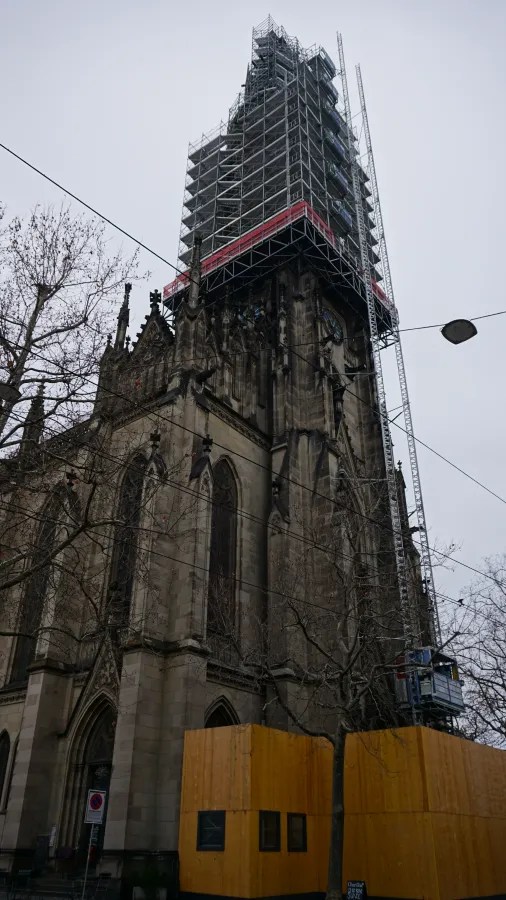 A tall gothic church spire encased in metal scaffolding for renovation.