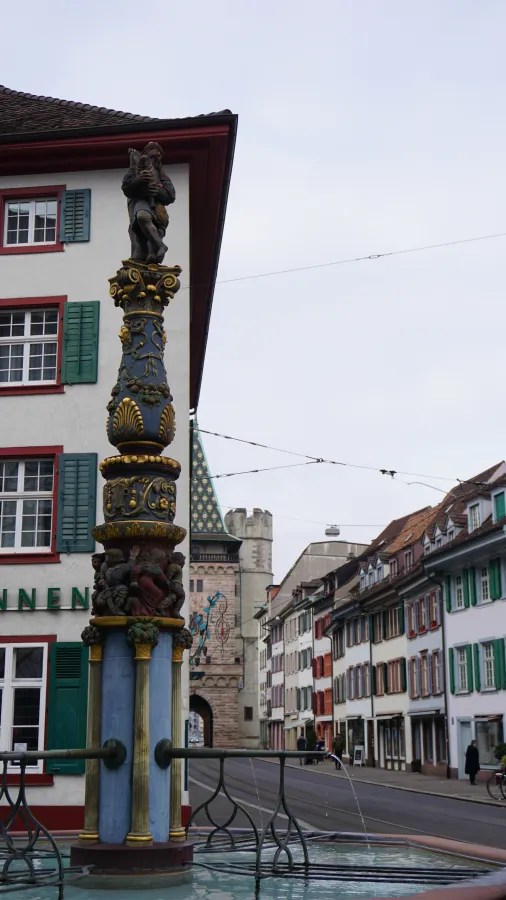Ornate fountain with a bagpiper statue in a European city street with historic buildings