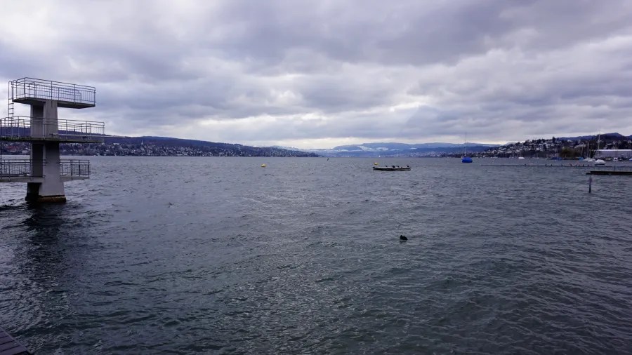 A multi-level diving platform on the shore of a large lake under an overcast sky.
