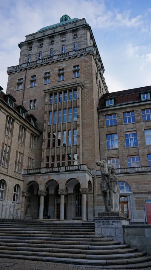 The main building of the University of Zurich with a stone statue and text UNIVERSITÄT ZÜRICH ZENTRUM.