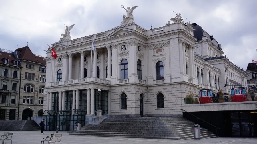 Neoclassical Zurich Opera House facade featuring ornate statues and a wide stone staircase.
