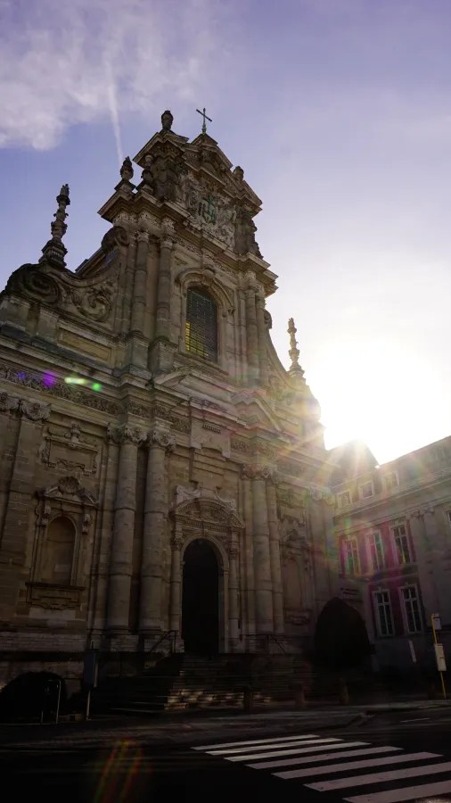 The facade of an ornate, historic stone church with sunlight and lens flares.