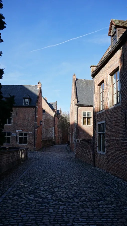 A narrow cobblestone street lined with historic red brick buildings under a clear blue sky