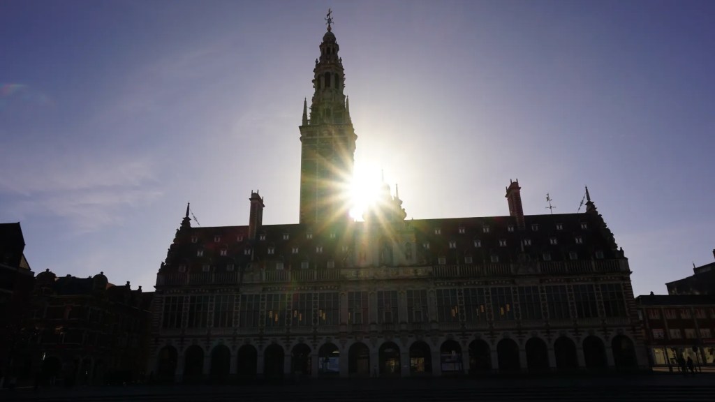 A large historic building with a tall tower silhouetted against a bright sunburst.