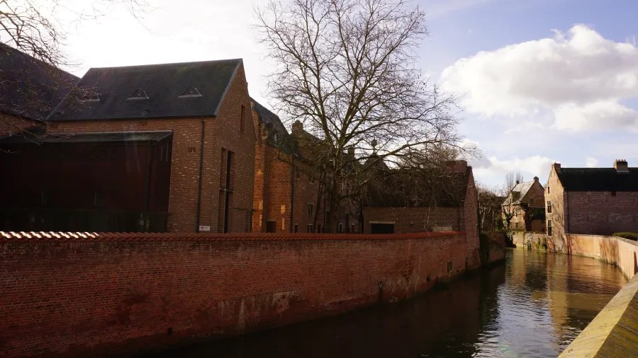 Historic red brick buildings and a wall alongside a quiet city canal.