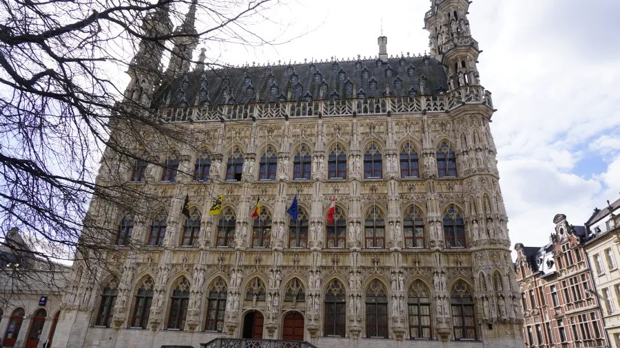 Ornate gothic town hall featuring many statues and flags on its detailed facade