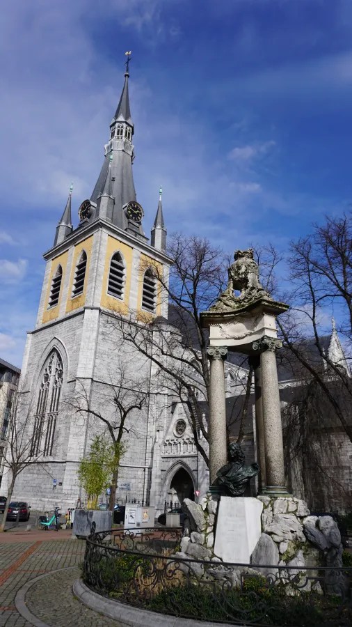 A historic stone cathedral with a tall spire and clock tower beside a classical monument.