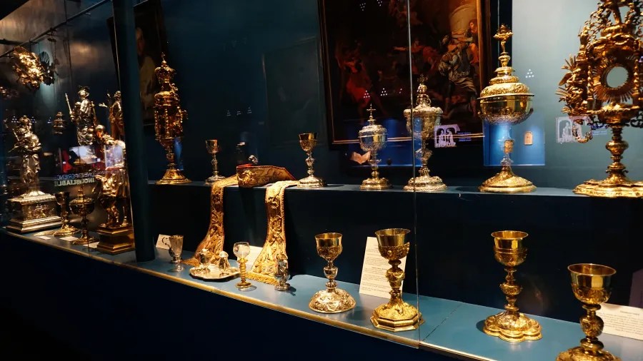 Ornate gold and silver religious artifacts, including chalices and monstrances, displayed in a museum case.
