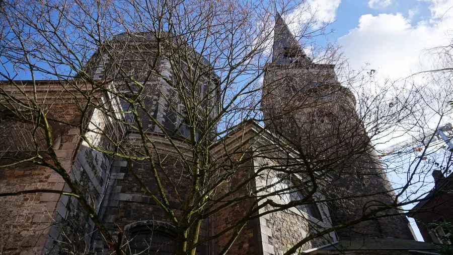 A low-angle view of a historic stone church building seen through bare tree branches.