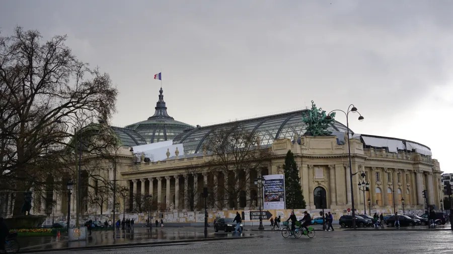 20230324_Frankreich_Paris (169) Large neoclassical building with glass dome and French flag, people and cyclists in front on rainy street