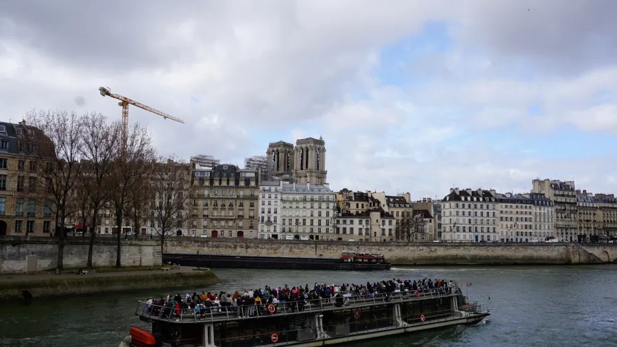 20230324_Frankreich_Paris (46) Tour boat with passengers on the Seine River in Paris with Notre-Dame Cathedral in the background under a cloudy sky