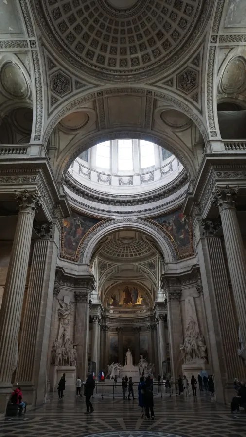 20230324_Frankreich_Paris (84) Interior of a grand neoclassical building with large columns, intricate ceiling dome, sculptures, and visitors walking inside