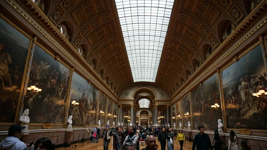20230325_Frankreich_Paris (139) Interior of a grand gallery with large historic paintings and many visitors walking under a glass ceiling