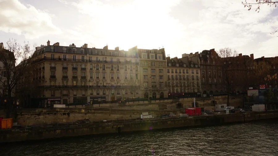 20230325_Frankreich_Paris (202) Historic buildings along the riverbank at sunset with sunlight filtering through clouds