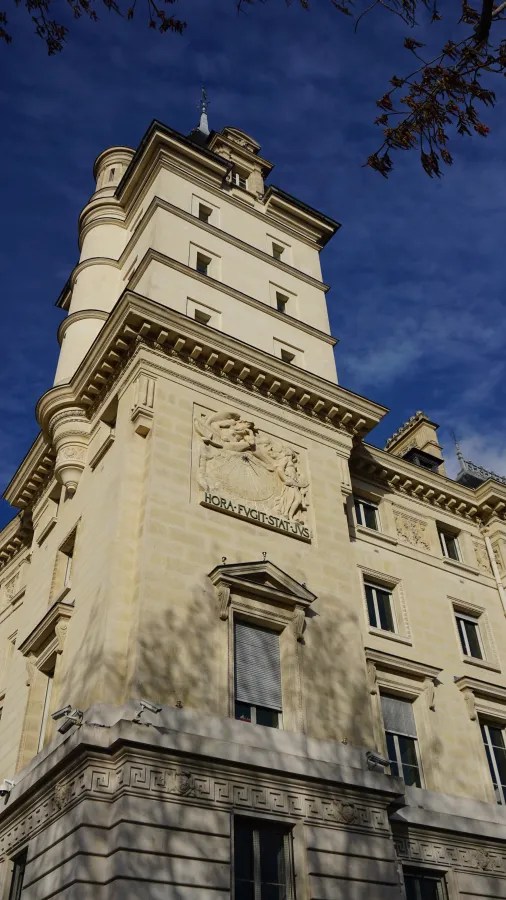 20230325_Frankreich_Paris (203) Cream-colored historic building with ornate architectural details and a Latin inscription on a relief plaque under a deep blue sky