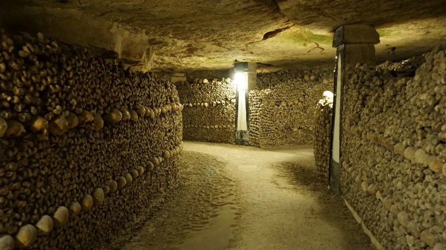 20230325_Frankreich_Paris (228) Underground corridor lined with stacked human skulls and bones illuminated by a single light