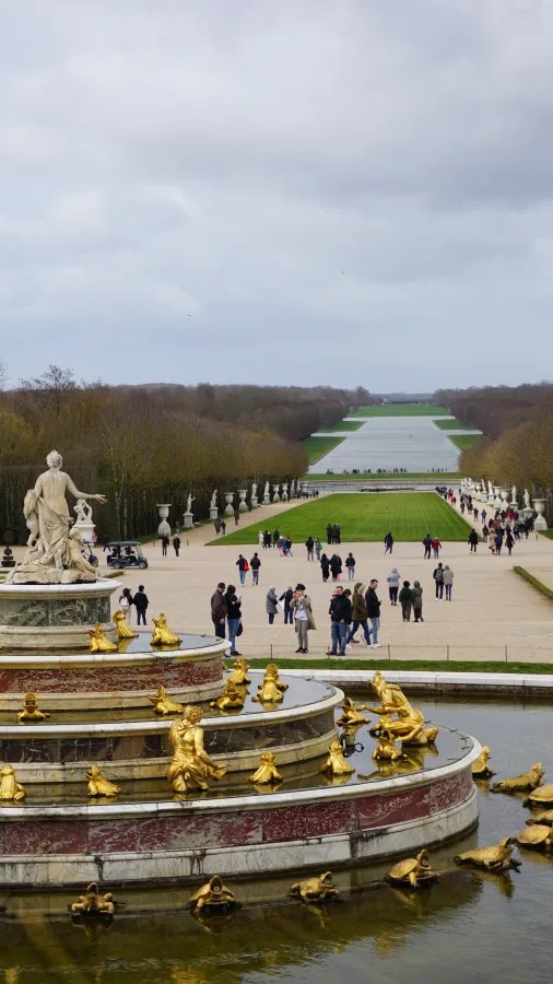 20230325_Frankreich_Paris (23) The Latona Fountain with gilded frog sculptures and statues in the gardens of the Palace of Versailles, people walking along a pathway leading to a large reflecting pool