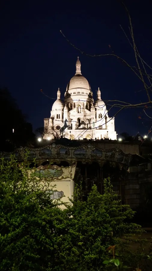 20230325_Frankreich_Paris (248) Illuminated Sacré-Cœur Basilica at night behind trees and a dark carousel