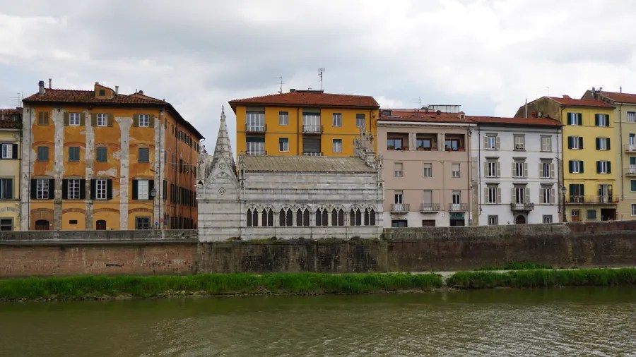 20230420_Italien_Toskana_Pisa (80) Row of historic riverside buildings with a small white chapel featuring gothic windows and a spire