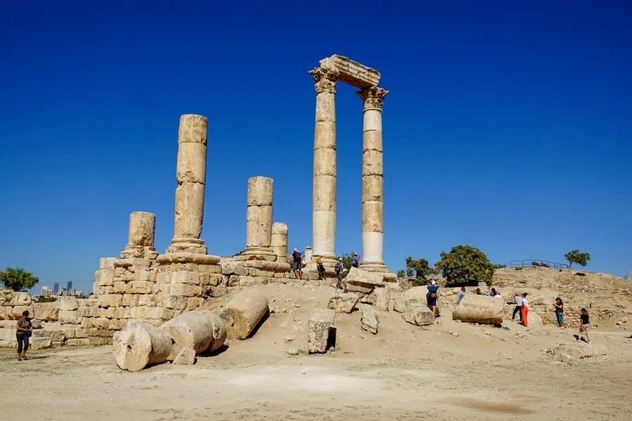 Ancient stone columns and ruins with tourists walking around under a clear blue sky