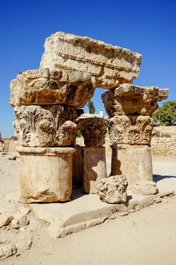 Ancient carved stone columns with floral motifs under bright blue sky in archaeological site