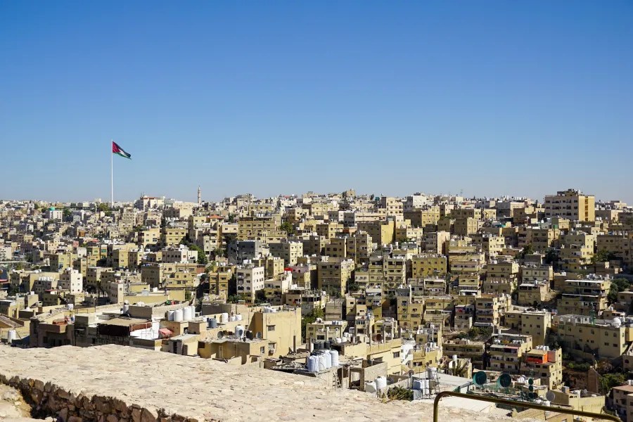 Cityscape of densely packed beige apartment buildings under a clear blue sky with a large flag on a tall pole