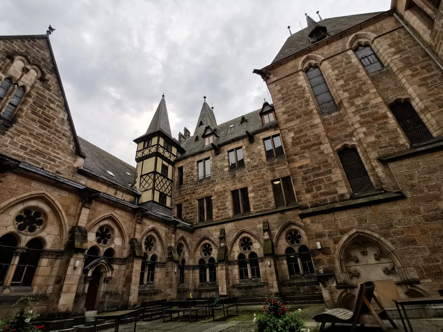 Courtyard of a historic stone building with arched windows and pointed towers under a cloudy sky