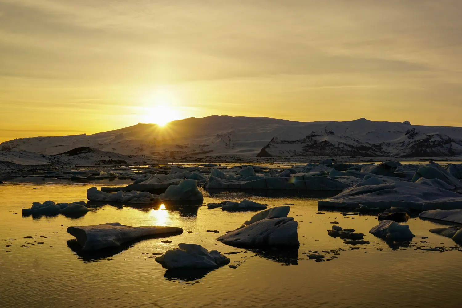 Sunset over icy lagoon with floating icebergs and snowy mountains