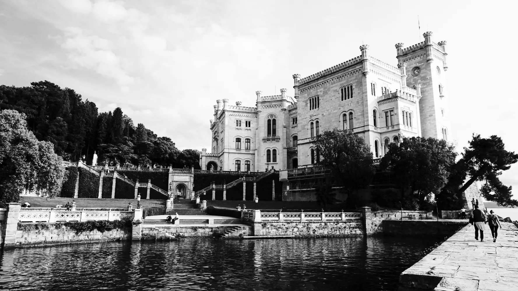 Large historic castle with towers and terraces by the water under cloudy sky